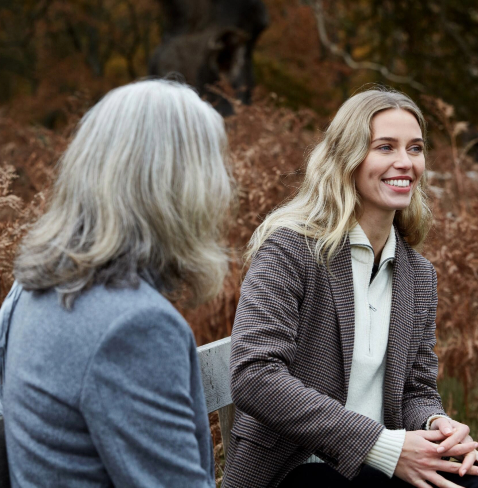 A mother and daughter talk while sitting on a bench in London's Richmond Park